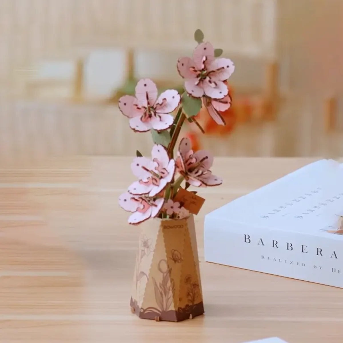 Rowood Sakura TW101 DIY wooden flower displayed on a warm tabletop as a pink cherry blossom craft decoration.