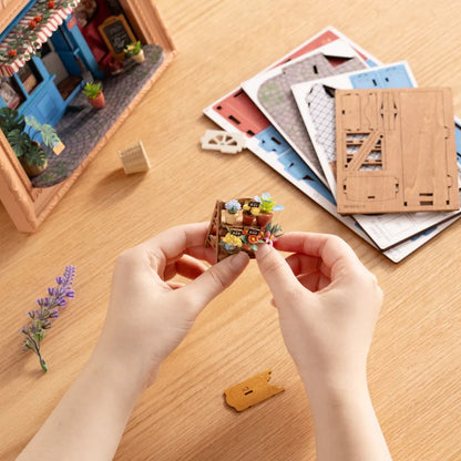 Rolife Daily Fresh Flower DP003 DIY assembly close-up showing hands building the miniature flower shelf with laser-cut parts