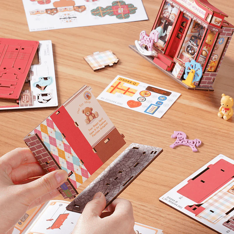 Rolife Whimsy Toy Shop DS044 assembly process with wooden parts, stickers, and instruction pieces.