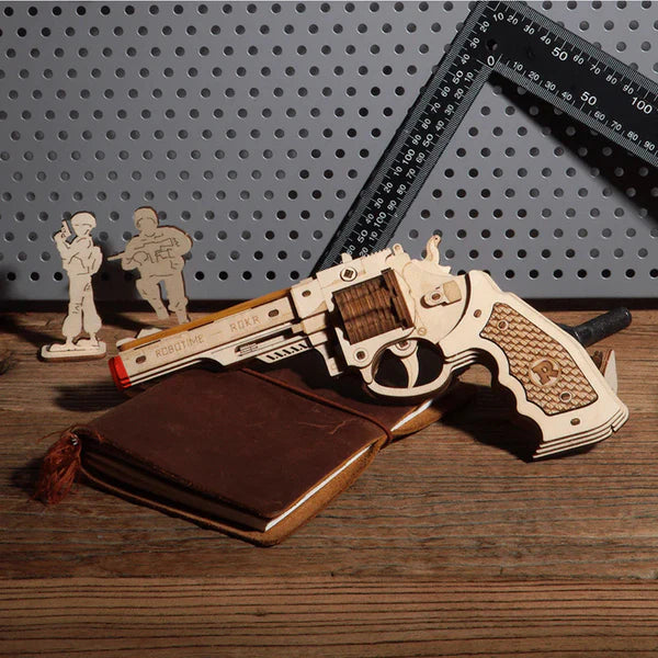 Decorative gun with wooden accents on a wooden surface, surrounded by small figures and a ruler.